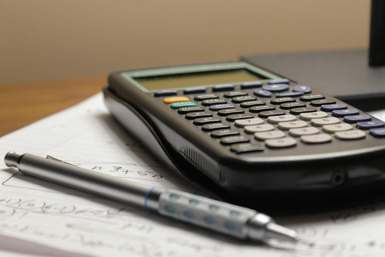 Calculadora e lapiseira apoiadas sobre uma folha com anotações feitas à mão, em uma mesa de madeira