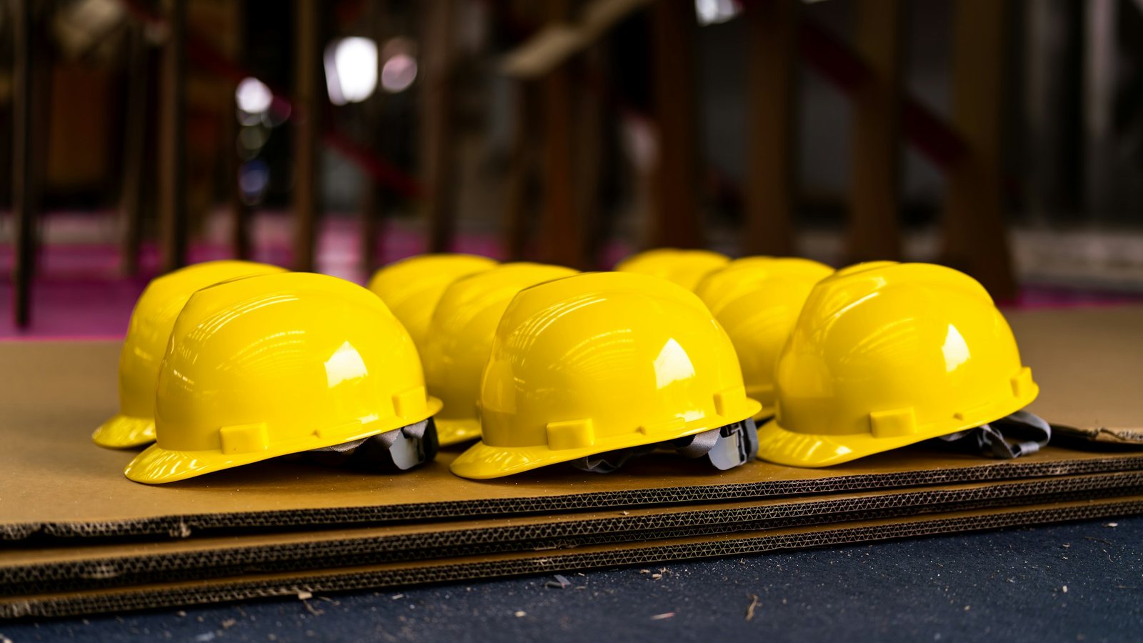 Capacetes de segurança amarelos alinhados sobre chapas de papelão em um galpão, prontos para a equipe