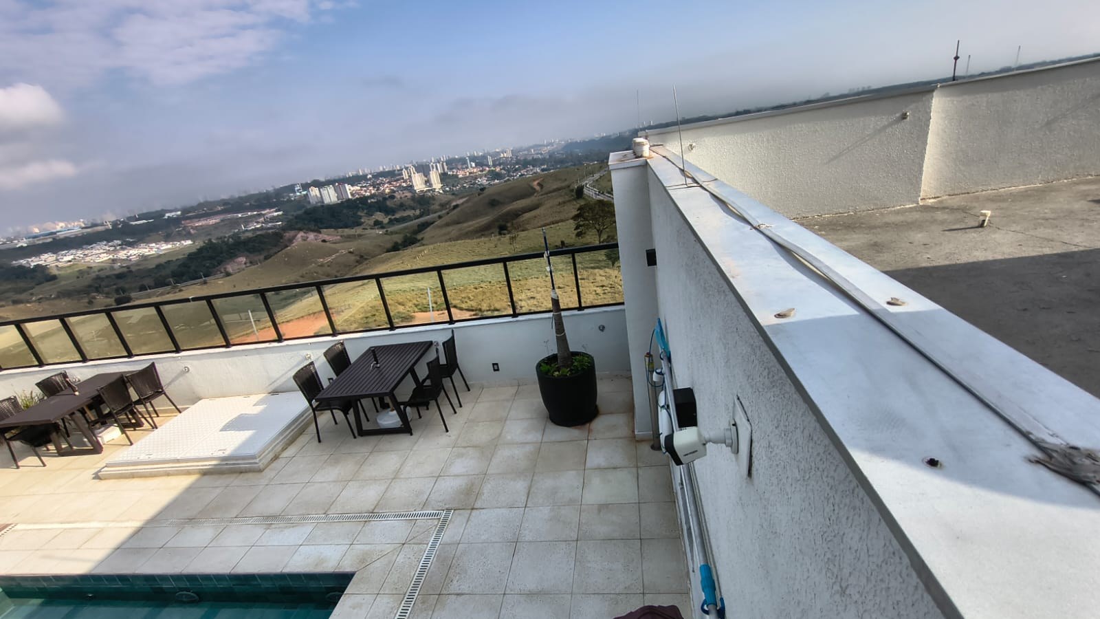 Cobertura de edifício residencial com o condutor de captação do para-raios correndo sobre a platibanda, com vista para morros e cidade ao fundo