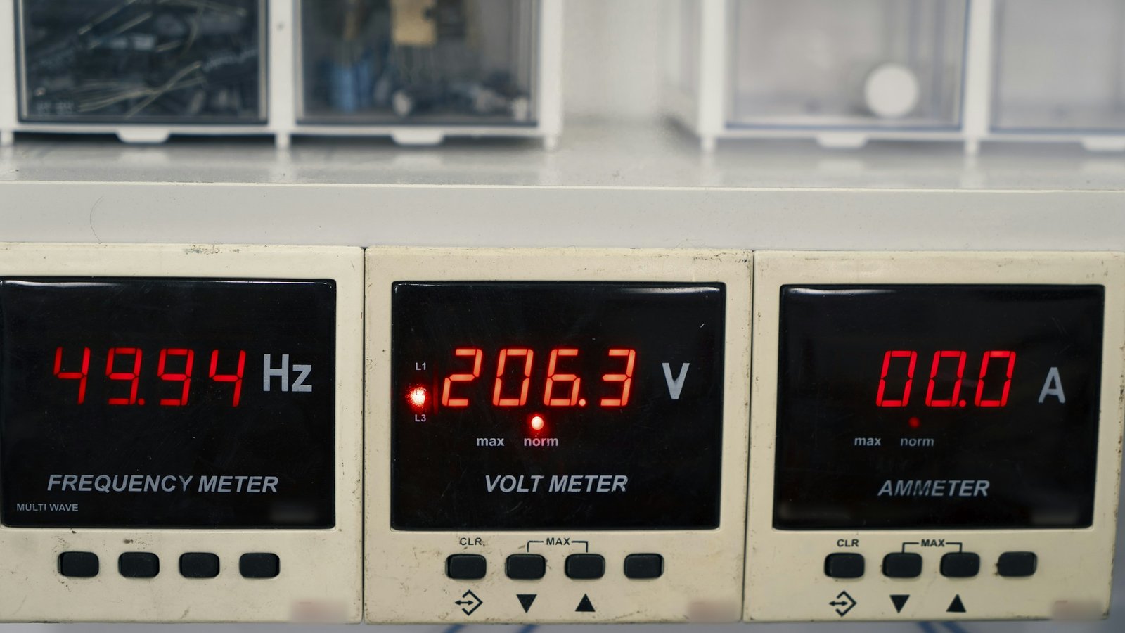 Três medidores digitais embutidos em painel, com leitura de frequência, de tensão marcando 206,3 volts e de corrente, em displays vermelhos