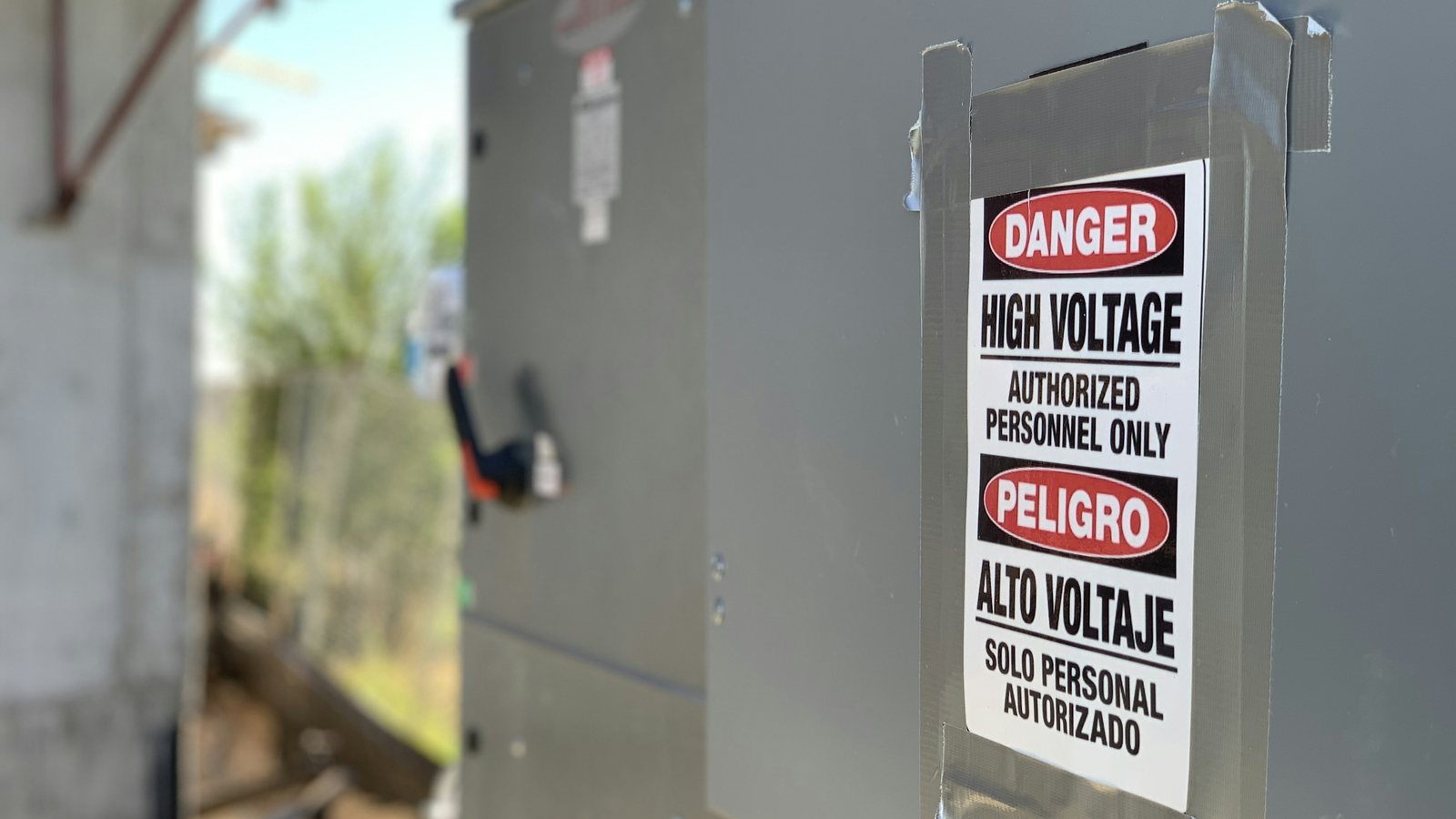 Gabinete elétrico metálico fechado em área externa, com placa de perigo de alta tensão avisando que o acesso é restrito a pessoal autorizado