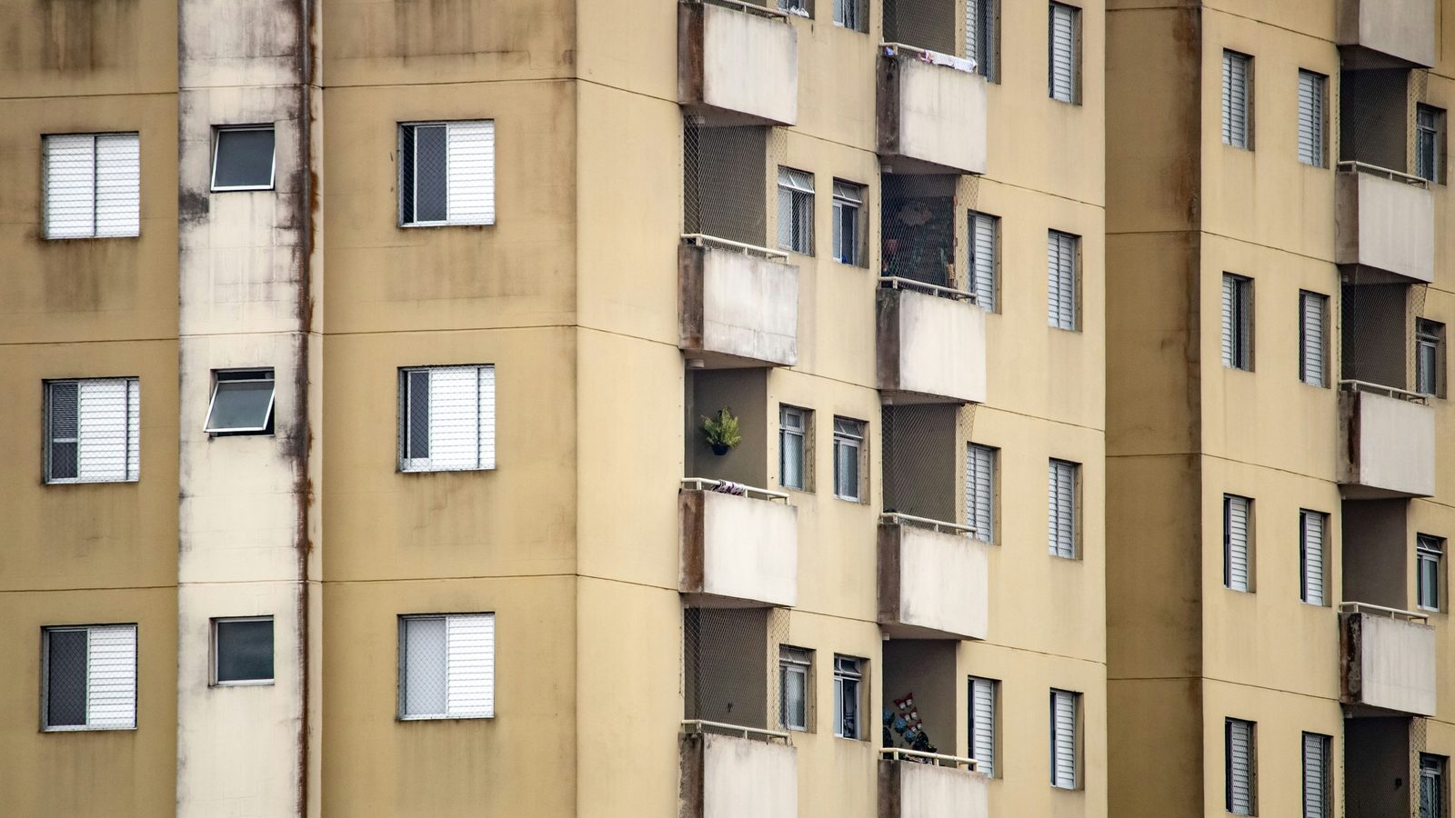 Fachada de prédio residencial antigo de vários andares, com pintura bege manchada pelo tempo, janelas com venezianas e varandas com tela de proteção
